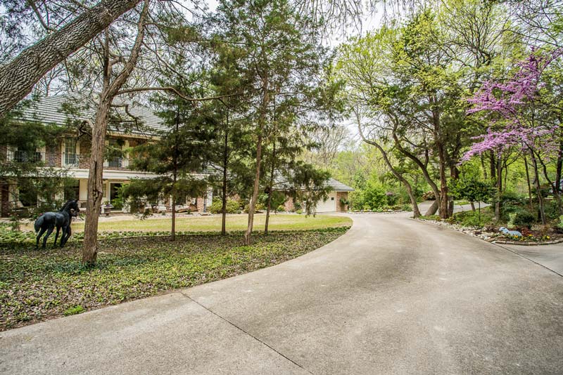 Beautiful driveway surrounded by trees leading to a two-story house